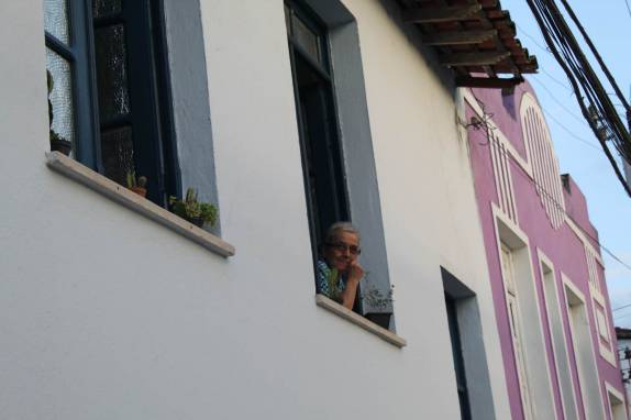 Senhora observa, de sua janela, a festa que passa pela rua em Cachoeira, no Recôncavo Baiano - BA